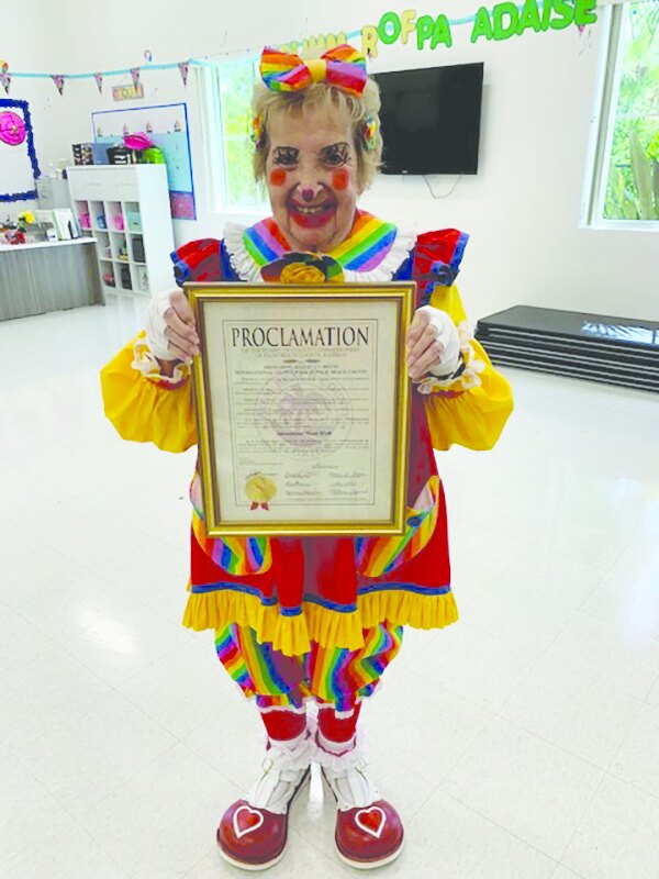 Clown Florabelle holding a framed International Clown Week proclamation