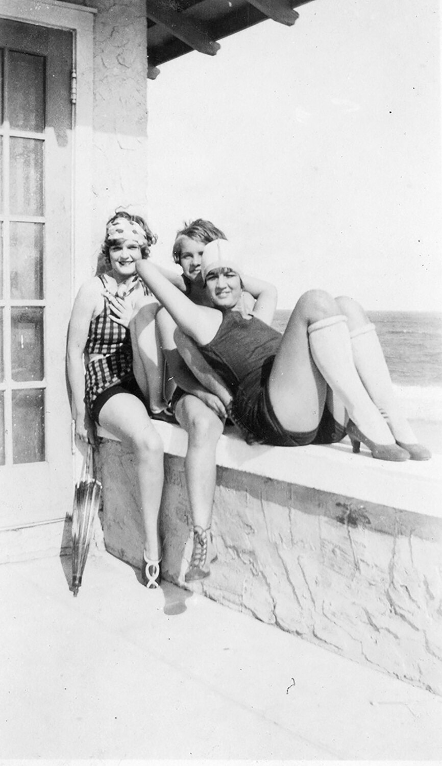 Two women in 1920s swimsuits seated on a wall at the Robbins house