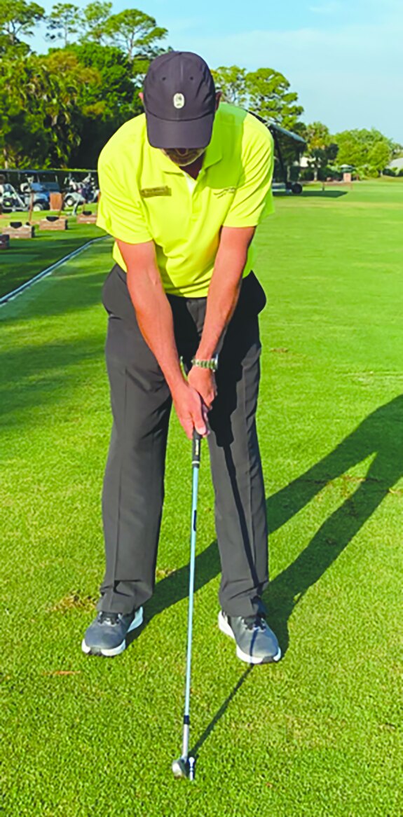 Golf instructor at address with an iron on a fairway demonstrating impact position