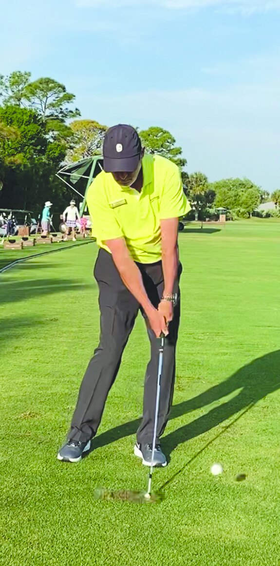 Golf instructor addressing a ball on the green demonstrating a low punch shot