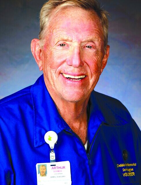 Arthur Dermer wearing a blue volunteer jacket and name badge