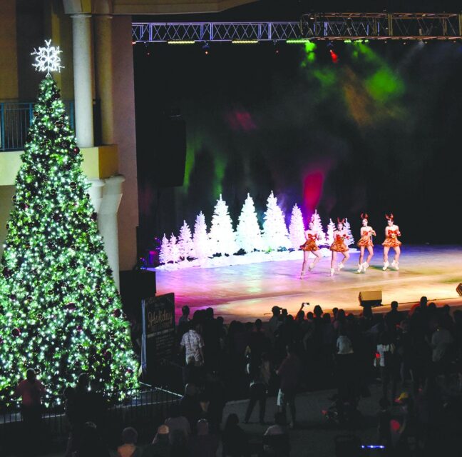 Lighted holiday tree beside skaters performing on an outdoor stage